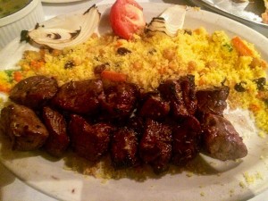 Lamb kabobs, couscous, a tomato on a plate.