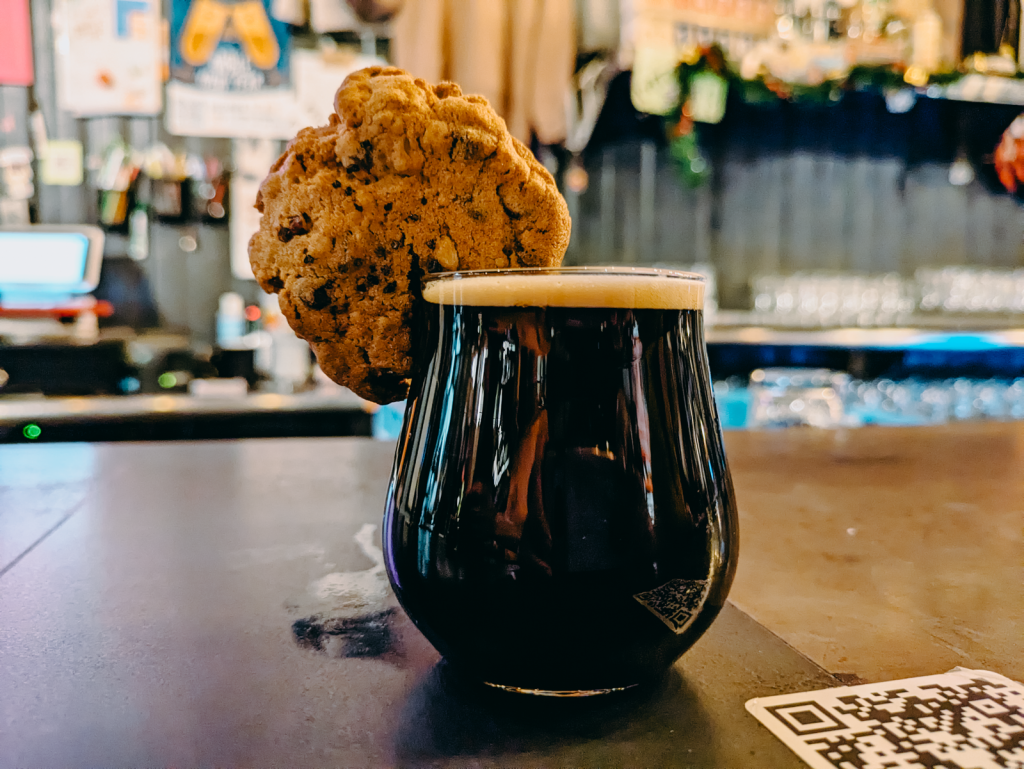 A small dark beer with an oatmeal cookie on the rim.