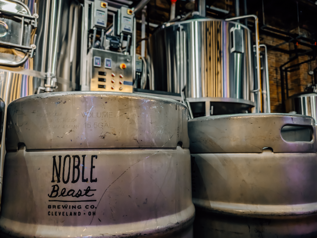 Two metal Noble Beast beer kegs in front of shiny brewing equipment.
